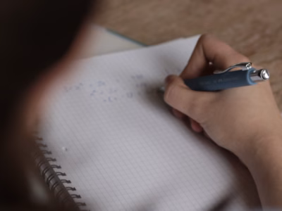 Person löst Mathematikaufgaben auf kariertem Papier