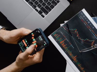 Person analysiert Finanzdiagramme auf Smartphone und Papier - Web Lernen Wirtschaftsmittelschule